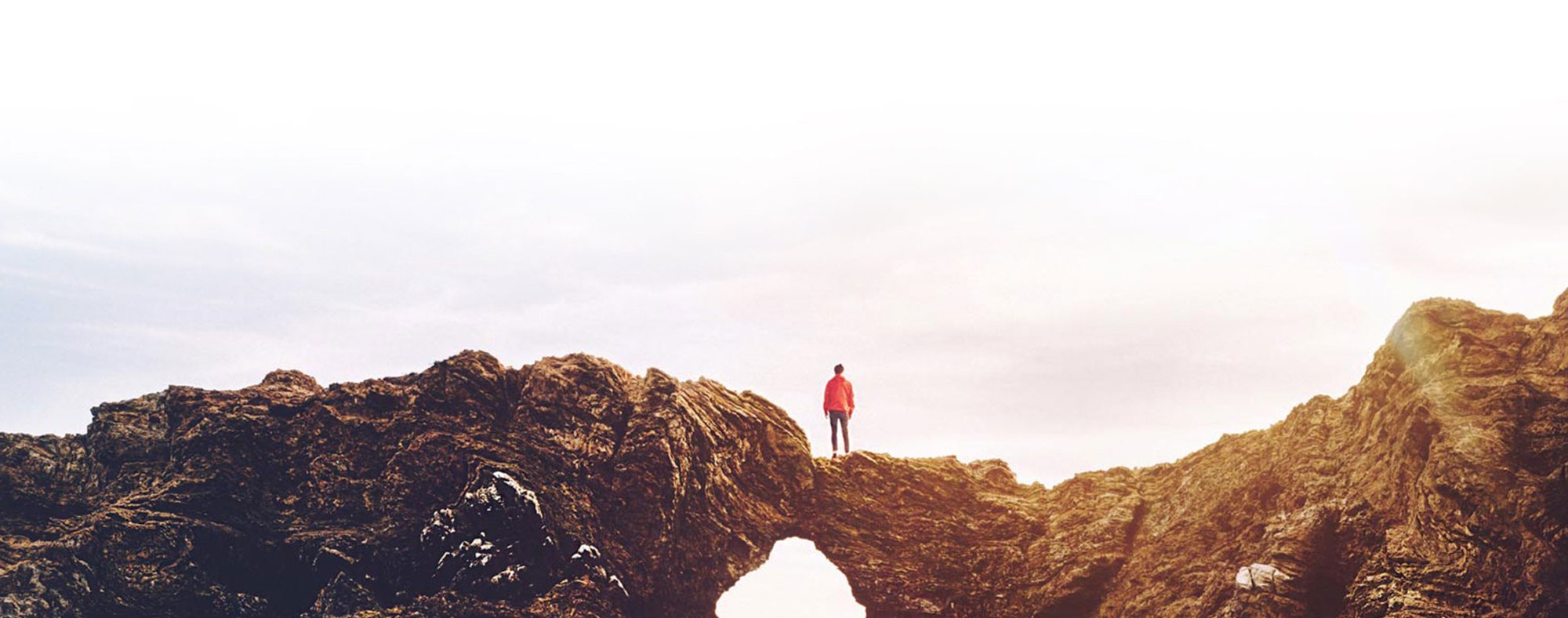 Traveler standing on a natural rock arch at sunset